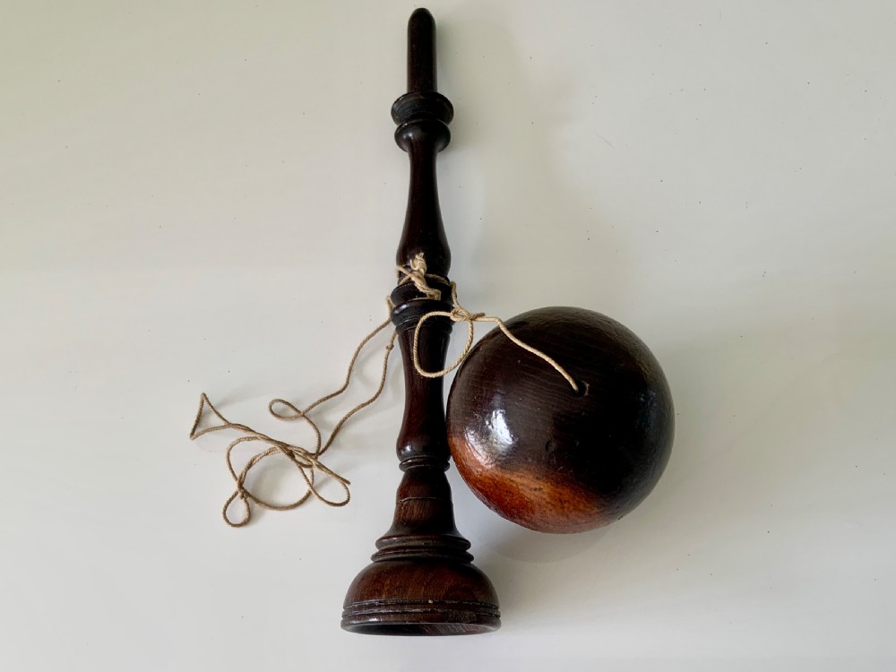 A lathe-turned dark wood bilboquet featuring a slender stem, attached cord, and a polished wooden sphere resting atop the spindle. View III