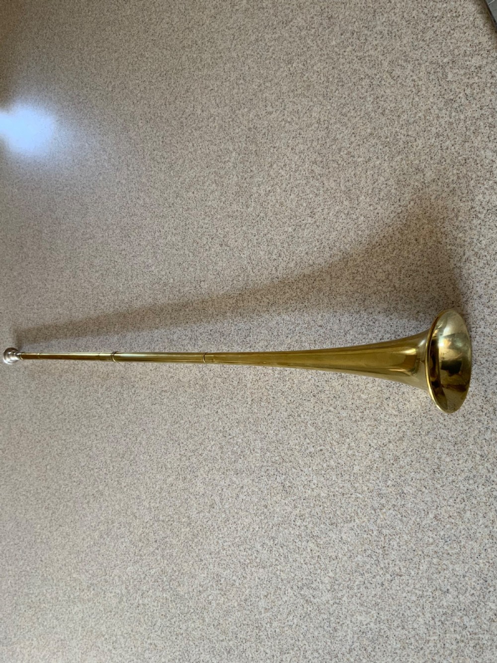 A long, straight late 19th-century brass coaching horn featuring a slender cylindrical body and a flared circular bell.