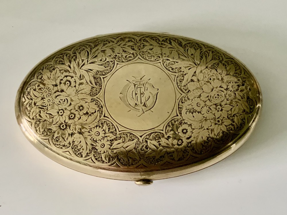 An oval brass Victorian sewing etui decorated with detailed floral engravings and a central monogrammed cartouche.