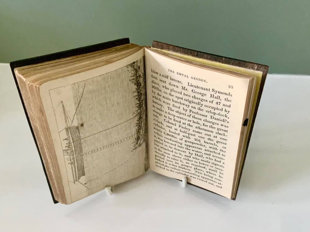 An open nineteenth-century book showing an engraved frontispiece illustration of a ship sinking on the left and a printed title page titled A Narrative of the Loss of the Royal George on the right. View VII