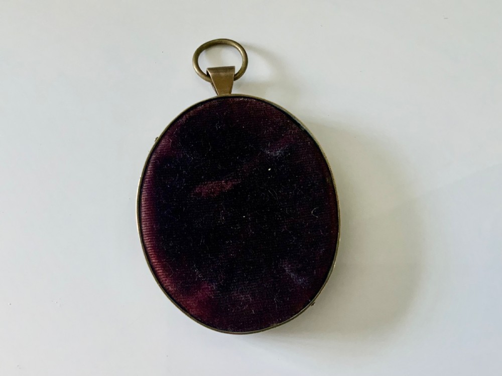 An oval antique portrait miniature depicting a young child with blonde hair, set within a brass frame with an upper suspension ring. View II