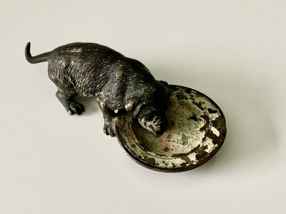 An antique Austrian cold-painted bronze sculpture depicting a small dog drinking from a shallow round bowl with remaining original paint.