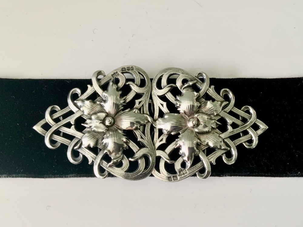 A two-piece sterling silver Art Nouveau belt buckle featuring floral openwork and sinuous curves mounted on a black band.