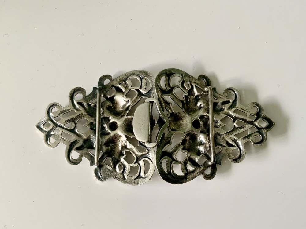 A two-piece sterling silver Art Nouveau belt buckle featuring floral openwork and sinuous curves mounted on a black band. View II