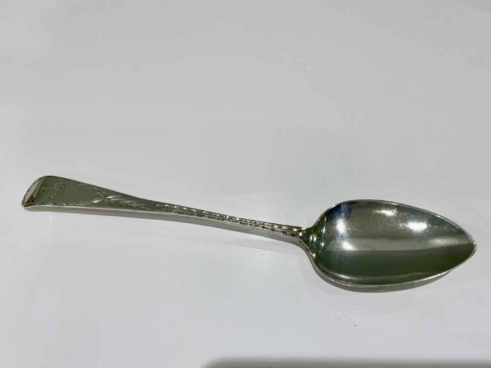 A Georgian sterling silver spoon featuring bright-cut hand engraving along the stem and an engraved monogram on the terminal.