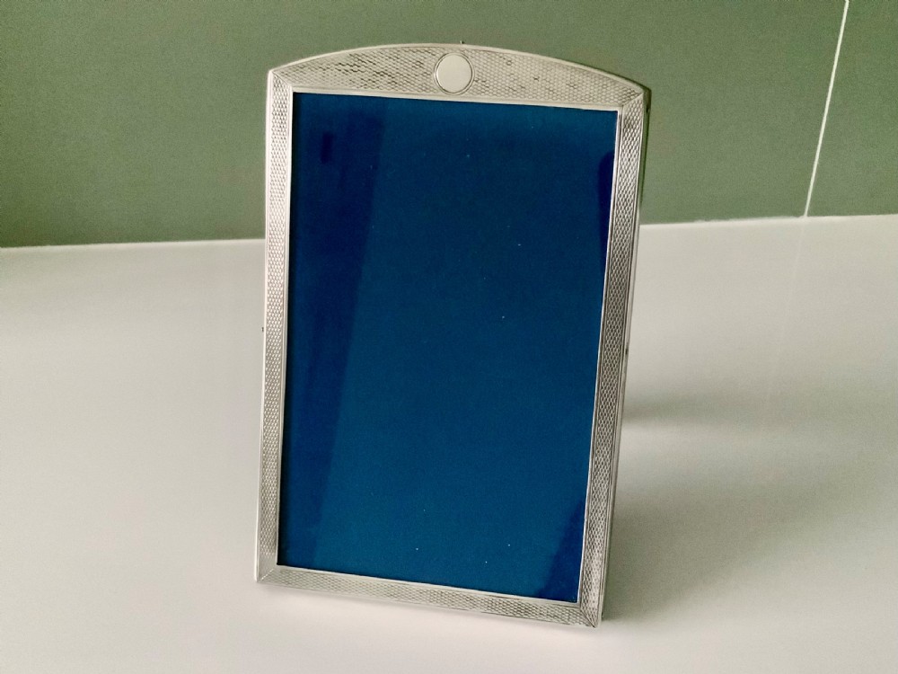 An upright Art Deco silver photograph frame with an arched top, engine-turned detailing, and a blue insert.
