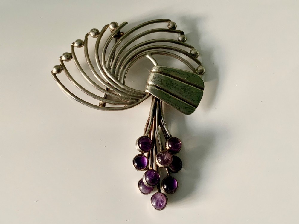 A Mexican sterling silver brooch designed with sweeping curved wires and hanging purple amethyst cabochons.