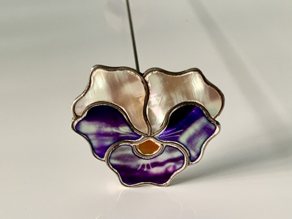 An early twentieth-century silver hatpin crafted in the shape of a pansy flower with iridescent mother-of-pearl top petals and purple enamelled lower petals.