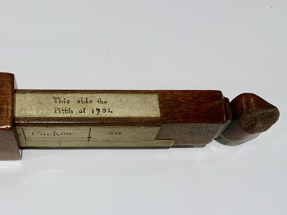 An elongated, rectangular wooden pitch pipe crafted from dark mahogany with a tapered mouthpiece at one end and a sound aperture. View II
