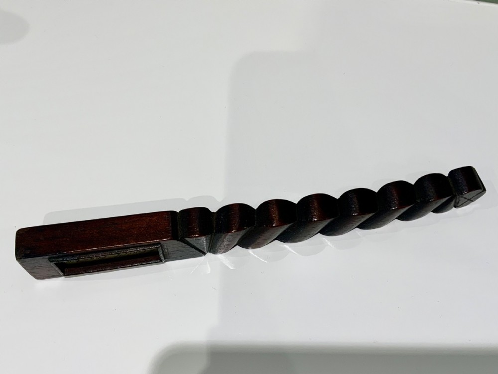 A dark carved wooden 19th-century knitting sheath featuring a heavy spiral-twisted shaft and an inset glass-covered handwritten inscription near the base. View V