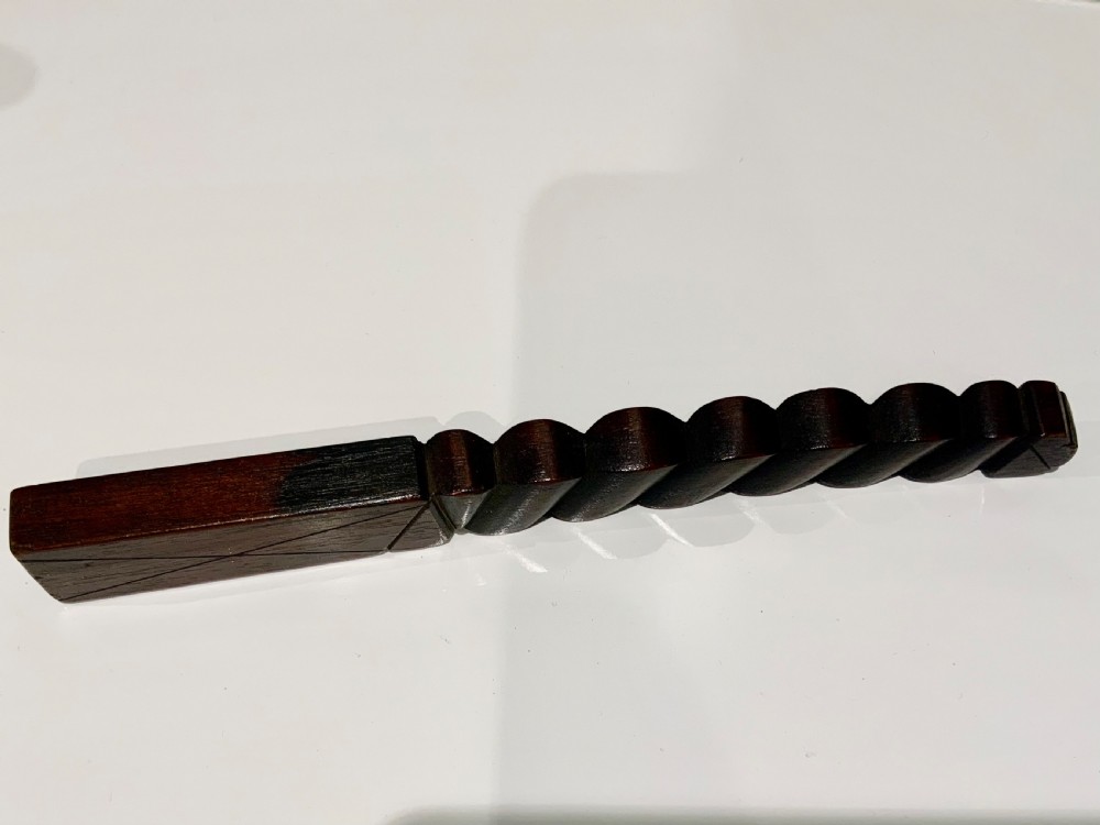 A dark carved wooden 19th-century knitting sheath featuring a heavy spiral-twisted shaft and an inset glass-covered handwritten inscription near the base. View VI