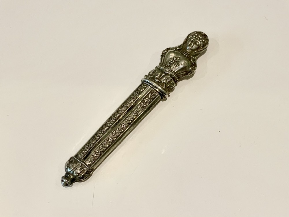 An early 19th-century silver needle case featuring figural bust detail at the top and floral embossed patterns along the cylindrical body.