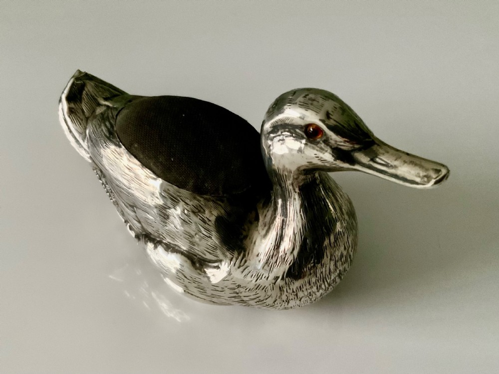 An Edwardian silver novelty pin cushion shaped like a resting duck, featuring detailed feather engraving, red glass eyes, and a dark velvet cushion on its back. View II