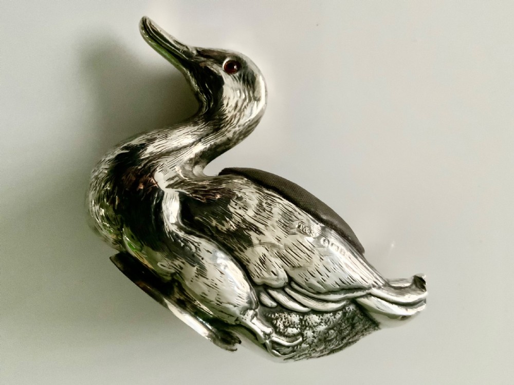 An Edwardian silver novelty pin cushion shaped like a resting duck, featuring detailed feather engraving, red glass eyes, and a dark velvet cushion on its back. View IV