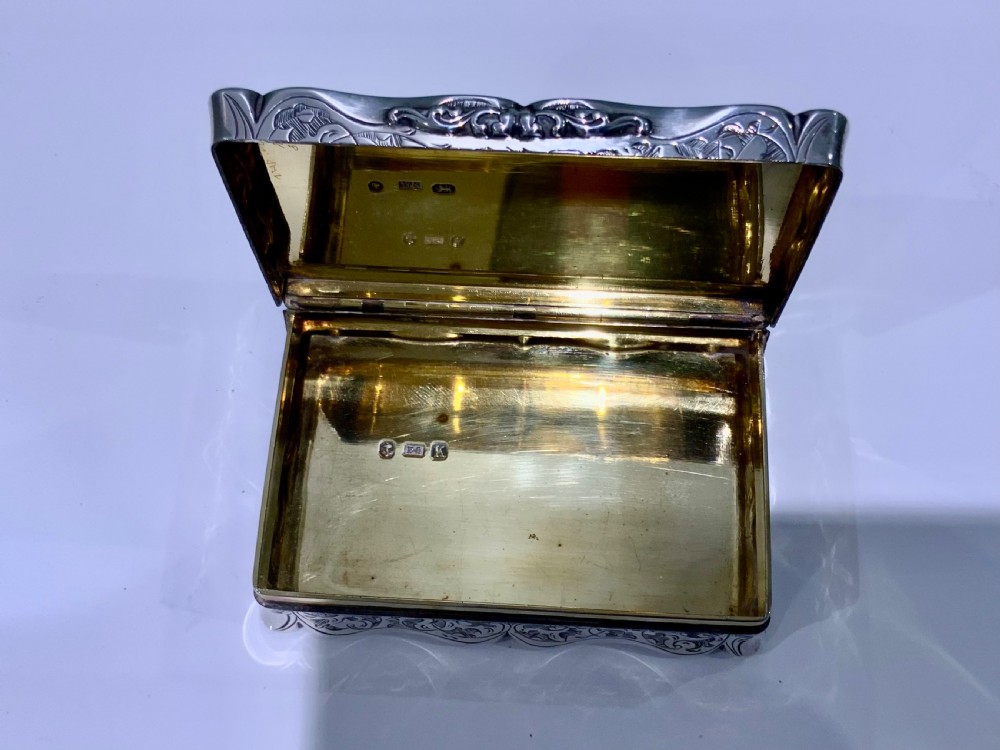 An ornate rectangular silver snuff box with intricate scroll engraving and a central inscription on the hinged lid. View VI