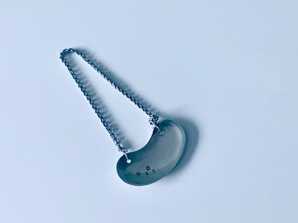 A crescent-shaped silver decanter label engraved with the word KIMMEL suspended from a silver chain. View II