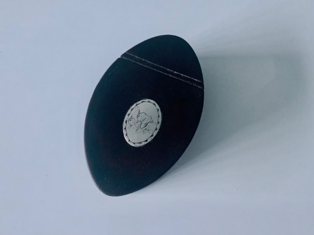 An oval dark brown leather Georgian snuff box featuring an engraved silver monogram cartouche on the lid.