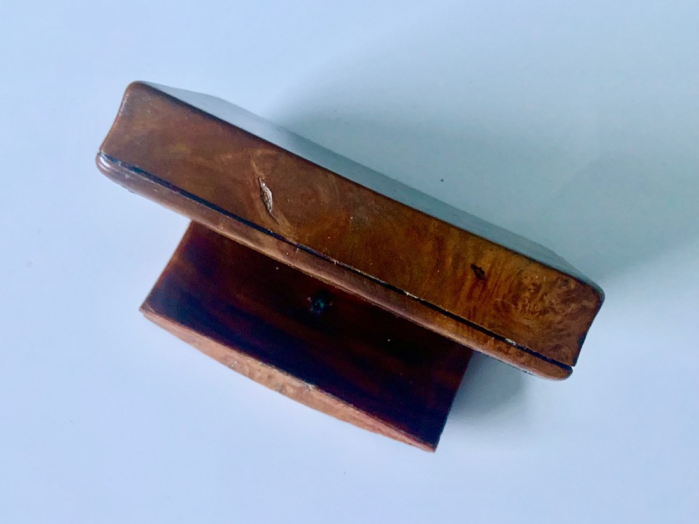 An overhead view of a rectangular antique burr wood snuff box featuring a distinctive swirling wood grain and a small engraved metal plaque set into the lid. View II