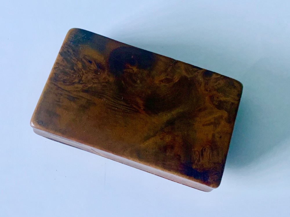 An overhead view of a rectangular antique burr wood snuff box featuring a distinctive swirling wood grain and a small engraved metal plaque set into the lid. View IV