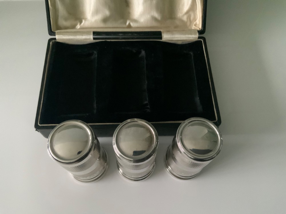An open black fitted case displaying three cylindrical Art Deco sterling silver canisters with engine-turned decoration and satin lining. View II