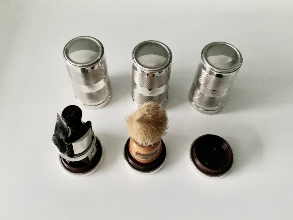 An open black fitted case displaying three cylindrical Art Deco sterling silver canisters with engine-turned decoration and satin lining. View IV