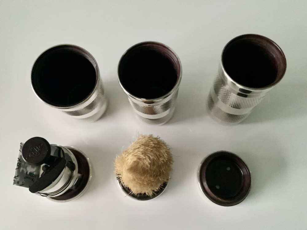 An open black fitted case displaying three cylindrical Art Deco sterling silver canisters with engine-turned decoration and satin lining. View V