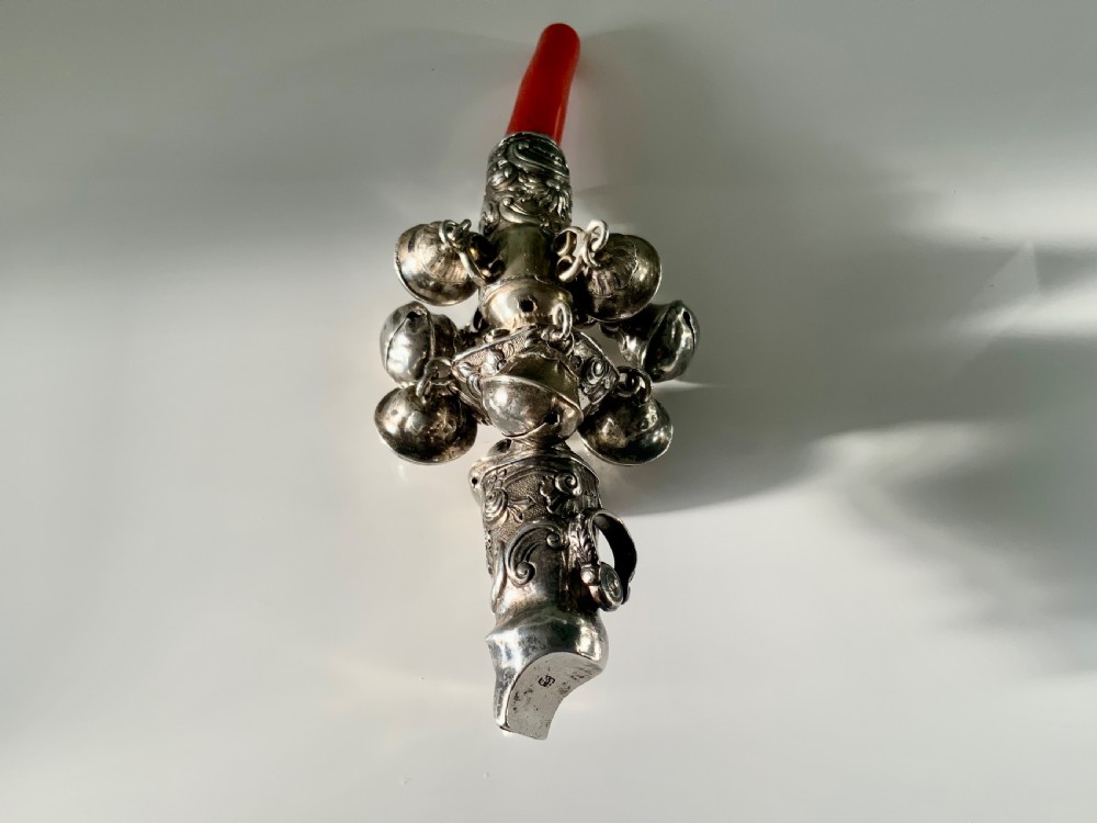An antique Georgian sterling silver baby rattle featuring detailed floral scrollwork, hanging bells, a whistle terminal, and a red coral teether handle. View III