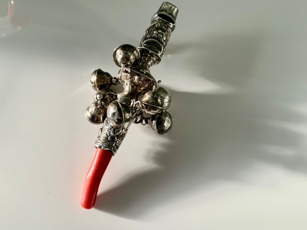 An antique Georgian sterling silver baby rattle featuring detailed floral scrollwork, hanging bells, a whistle terminal, and a red coral teether handle. View IV