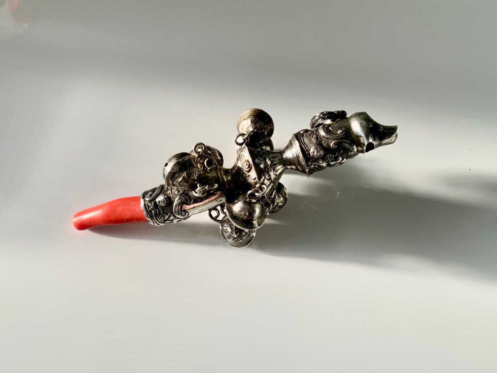 An antique Georgian sterling silver baby rattle featuring detailed floral scrollwork, hanging bells, a whistle terminal, and a red coral teether handle. View V