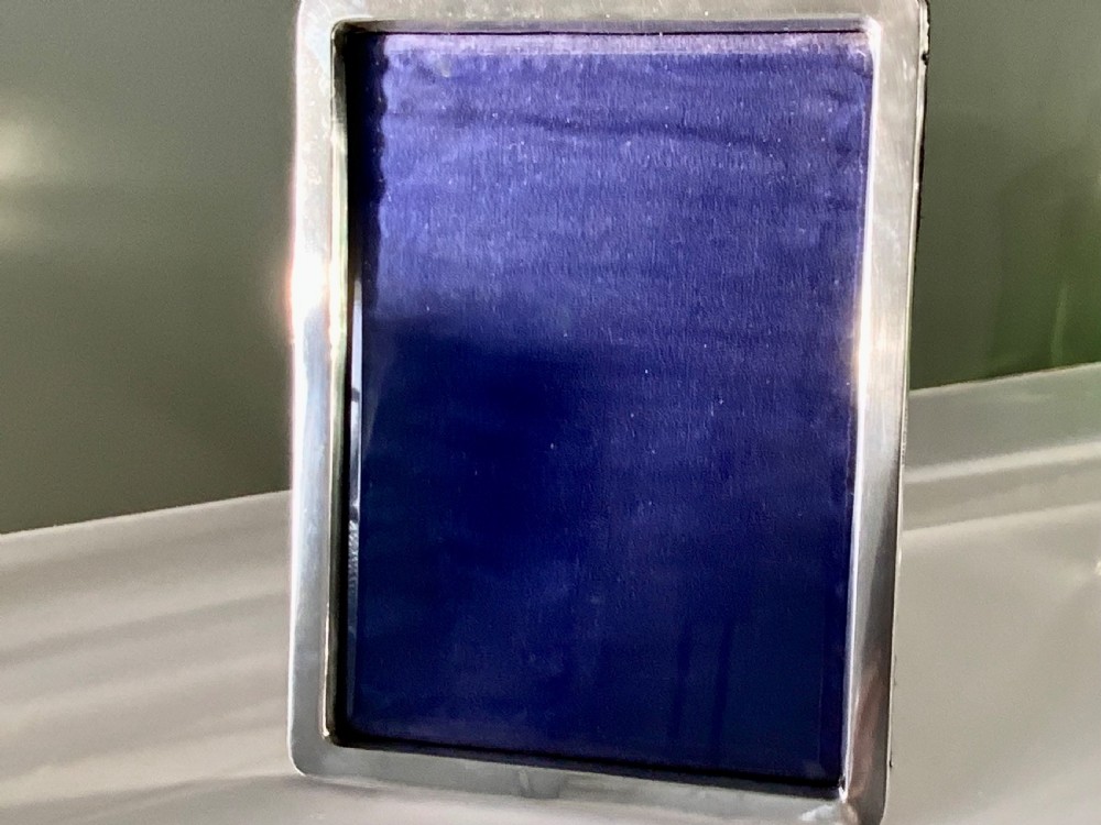 A rectangular sterling silver photograph frame with a plain polished border and dark blue velvet backing.