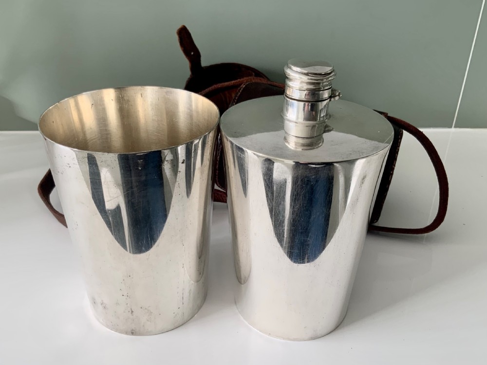 A Victorian silver-plated cylindrical flask engraved with initials alongside a dark brown leather carrying case with a shoulder strap. View VII