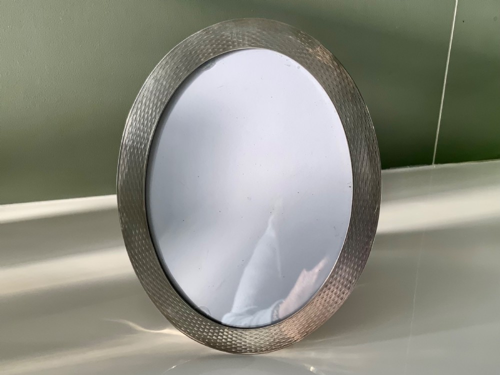 An early 20th-century oval silver photograph frame featuring an engine-turned textured border.