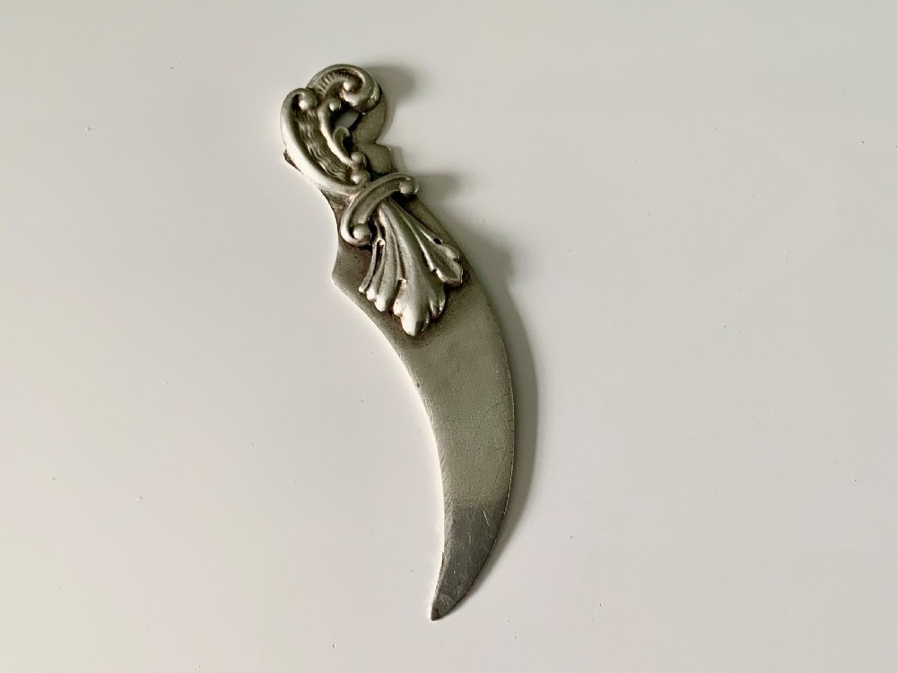 A curved sterling silver bookmark and page opener featuring repousse leaf and scroll detailing on the handle.