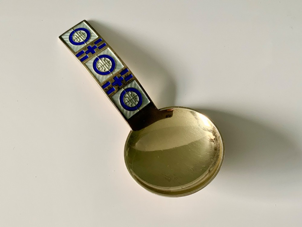A David Andersen sterling silver gilt caddy spoon with a round bowl and a flat geometric blue and white guilloche enamel handle.
