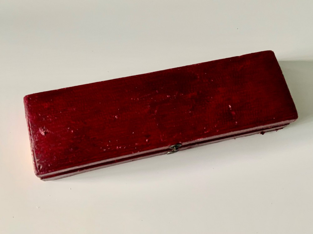 A boxed Georgian sterling silver childs knife and three-tined fork with shell motifs on the handles, displayed below a red fitted presentation case. View IV