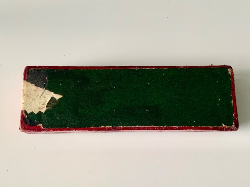 A boxed Georgian sterling silver childs knife and three-tined fork with shell motifs on the handles, displayed below a red fitted presentation case. View V