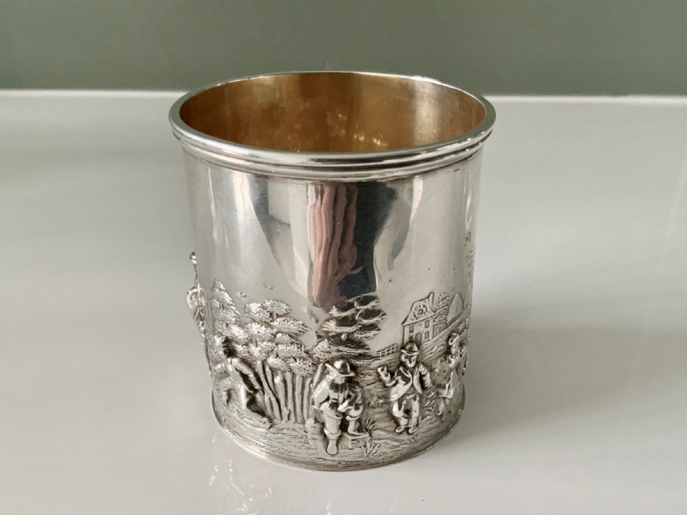 A small sterling silver christening mug decorated with embossed pastoral figures and a church landscape, featuring an angular side handle. View II