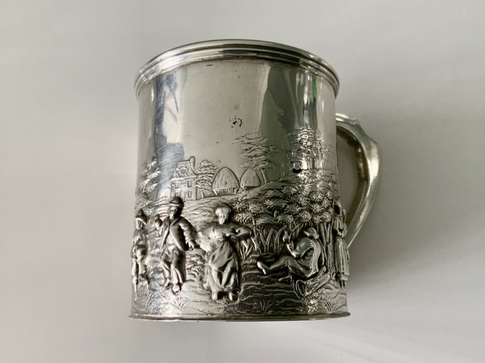 A small sterling silver christening mug decorated with embossed pastoral figures and a church landscape, featuring an angular side handle. View III