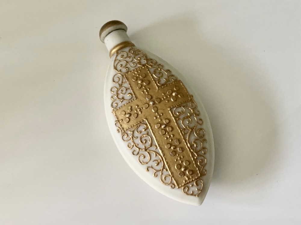 An elongated white parian ware scent bottle featuring raised gilded scrollwork and a central cross design.