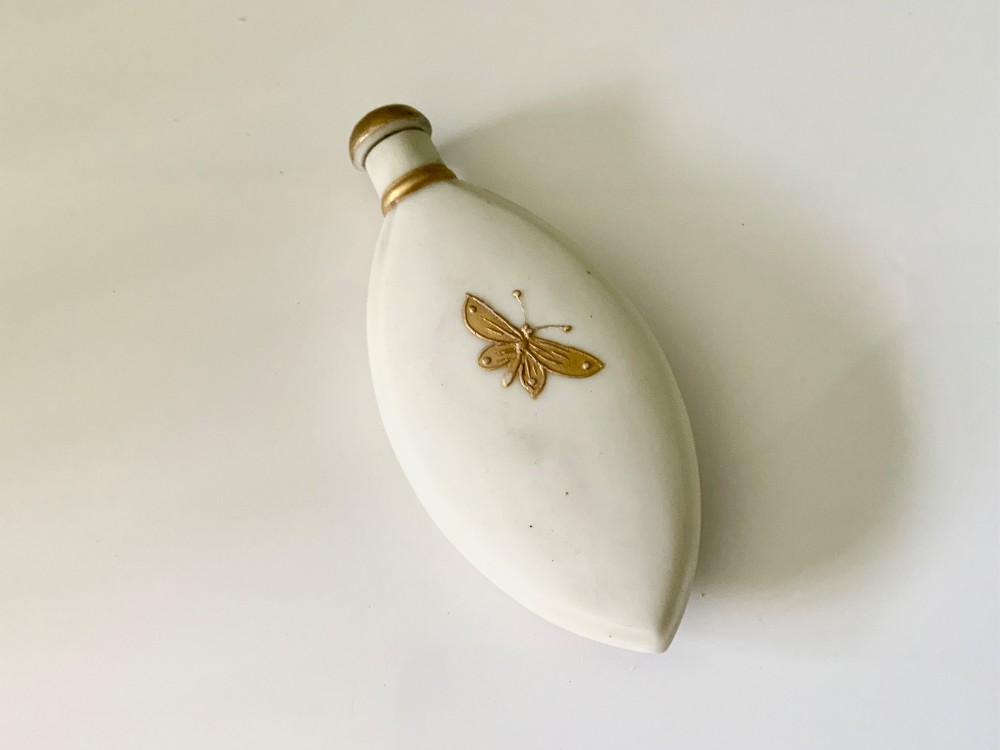 An elongated white parian ware scent bottle featuring raised gilded scrollwork and a central cross design. View II