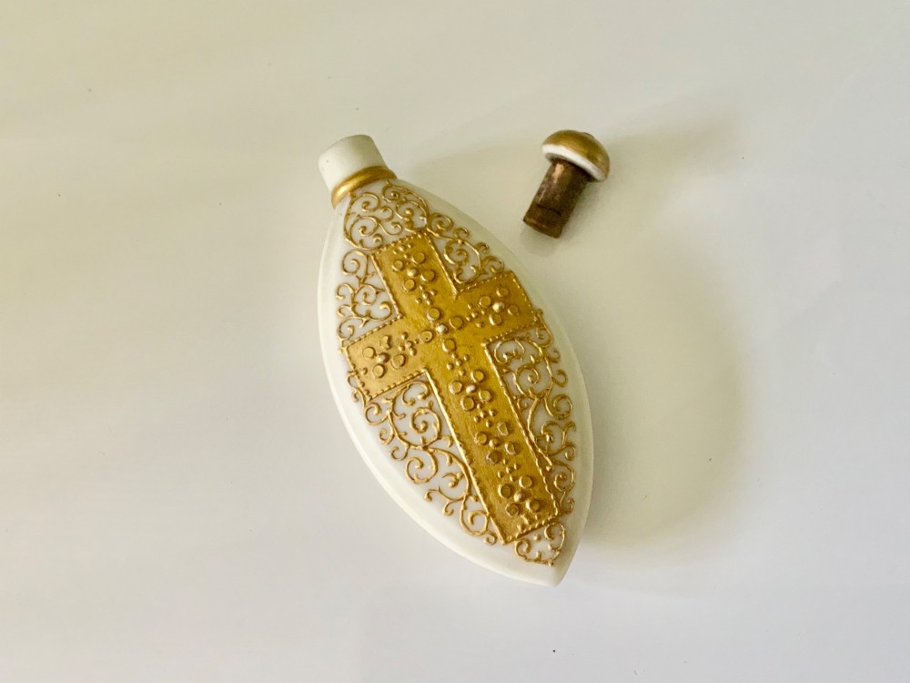 An elongated white parian ware scent bottle featuring raised gilded scrollwork and a central cross design. View III