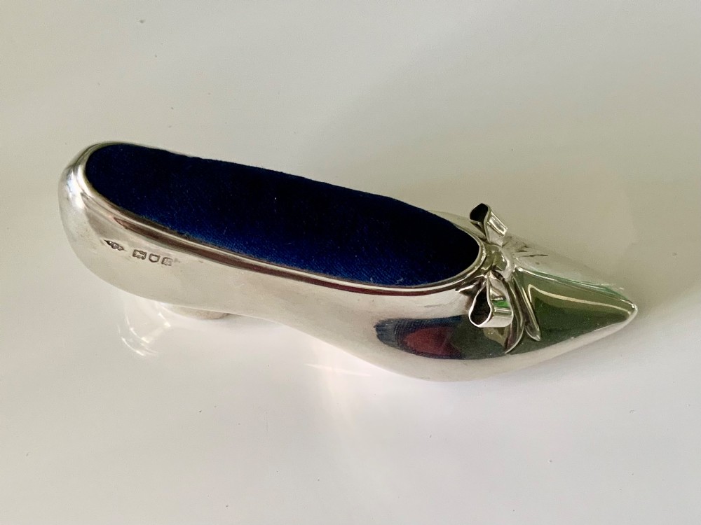 A silver novelty pin cushion shaped like a pointed shoe featuring a silver bow motif on the vamp and a navy blue velvet interior insert. View II