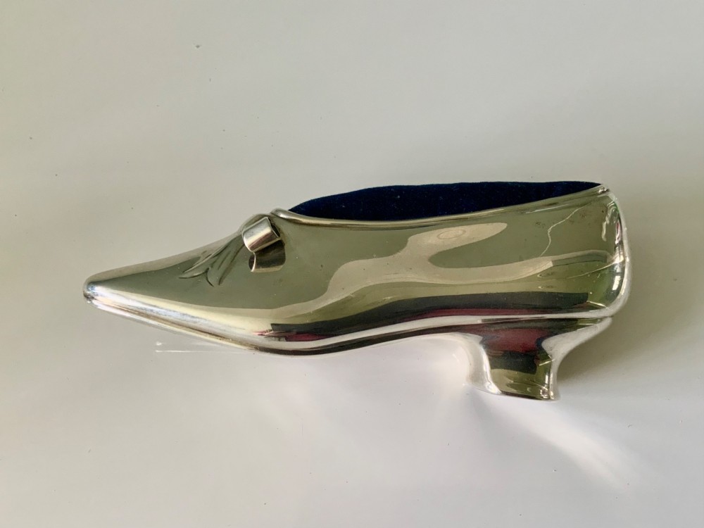 A silver novelty pin cushion shaped like a pointed shoe featuring a silver bow motif on the vamp and a navy blue velvet interior insert. View IV