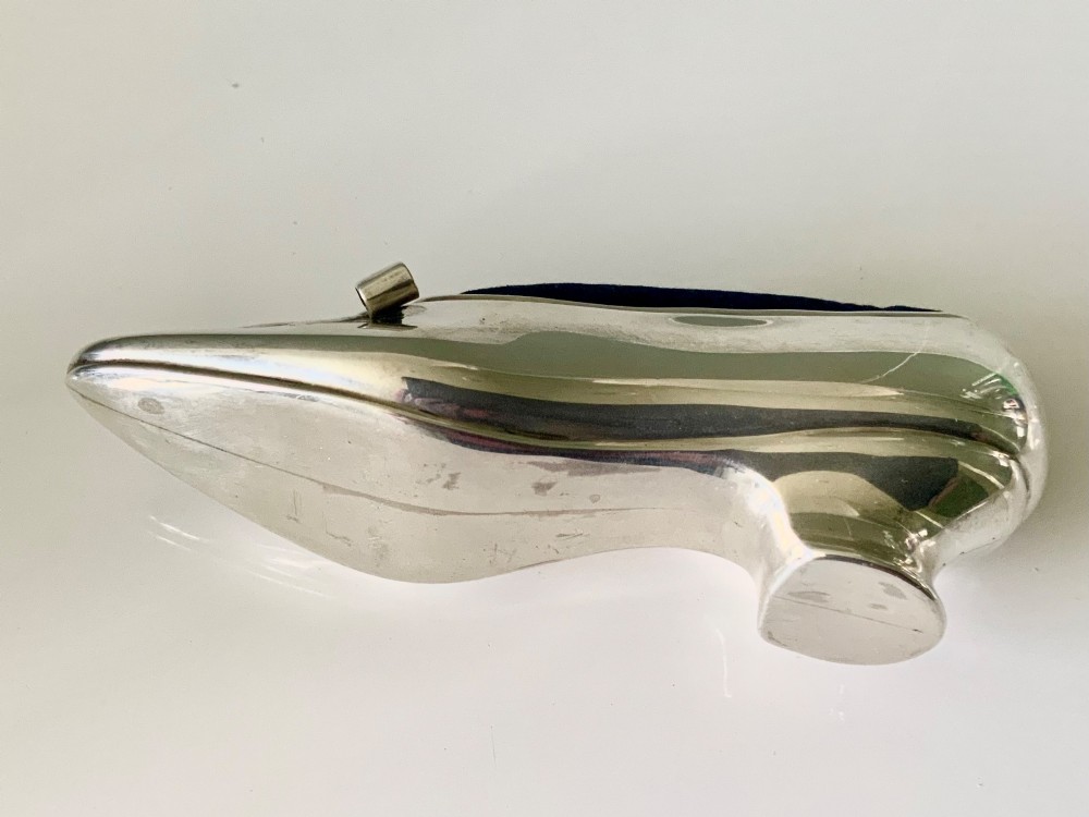 A silver novelty pin cushion shaped like a pointed shoe featuring a silver bow motif on the vamp and a navy blue velvet interior insert. View V