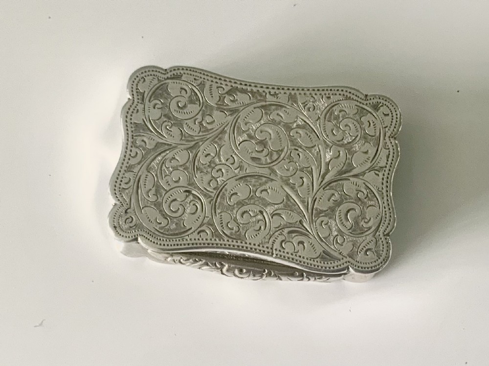 A rectangular sterling silver snuff box with a hinged lid, featuring detailed foliate engraving, a scalloped border, and a plain central circular cartouche. View II