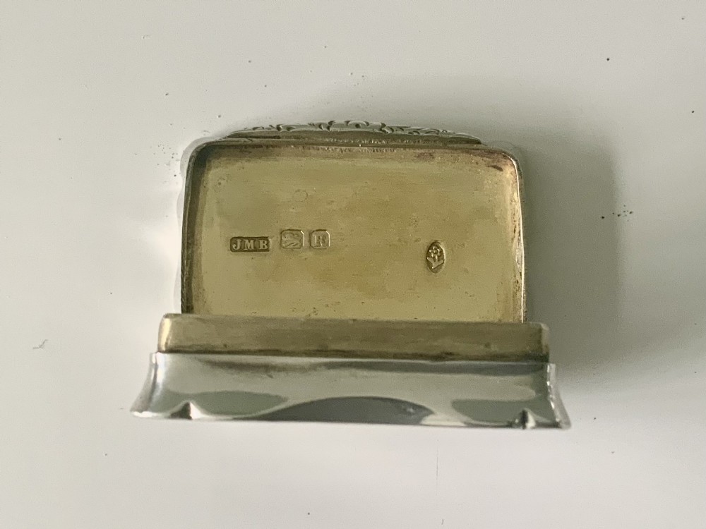 A rectangular sterling silver snuff box with a hinged lid, featuring detailed foliate engraving, a scalloped border, and a plain central circular cartouche. View III
