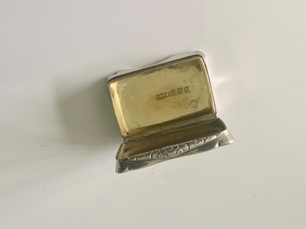 A rectangular sterling silver snuff box with a hinged lid, featuring detailed foliate engraving, a scalloped border, and a plain central circular cartouche. View IV