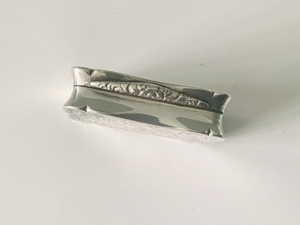 A rectangular sterling silver snuff box with a hinged lid, featuring detailed foliate engraving, a scalloped border, and a plain central circular cartouche. View V