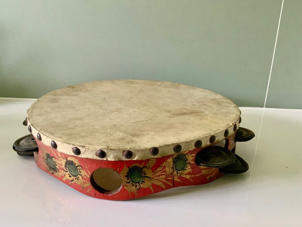 An antique Regency circular wooden tambourine featuring hand-painted red and gold floral patterns, metal jingles set into the rim, and a taut vellum head secured with brass studs.