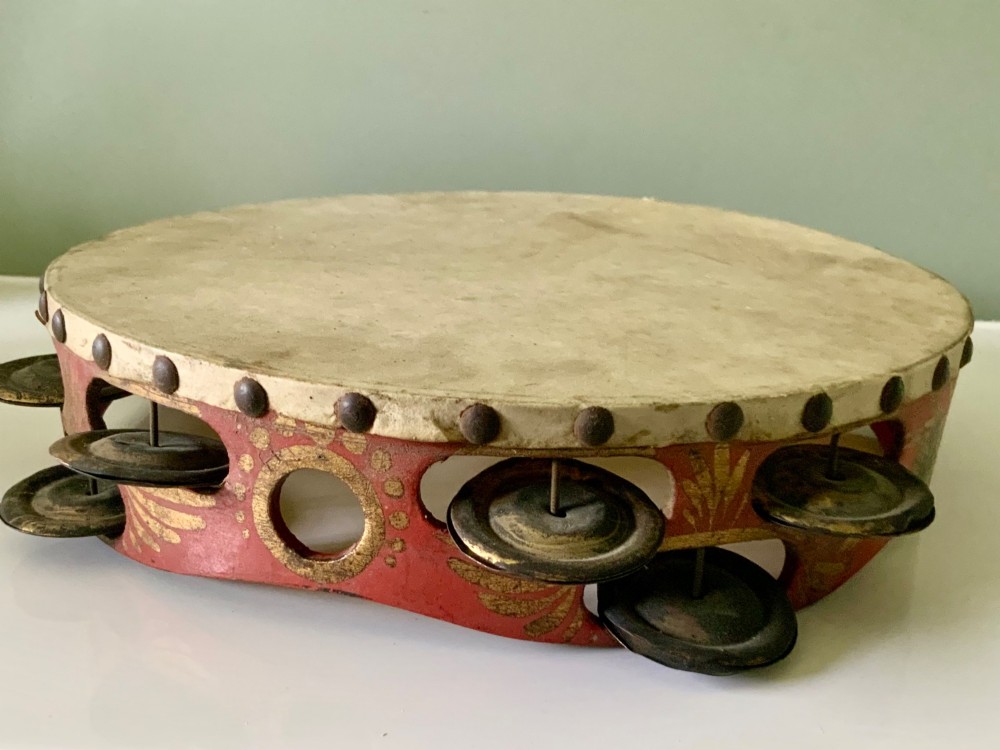 An antique Regency circular wooden tambourine featuring hand-painted red and gold floral patterns, metal jingles set into the rim, and a taut vellum head secured with brass studs. View II